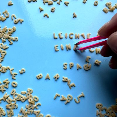 Rundes Foto, das Suppen-Buchstaben auf hellblauem Hintergrund zeigt. Es steht mit den Buchstaben geschrieben: Leichte Einfache Sprache.